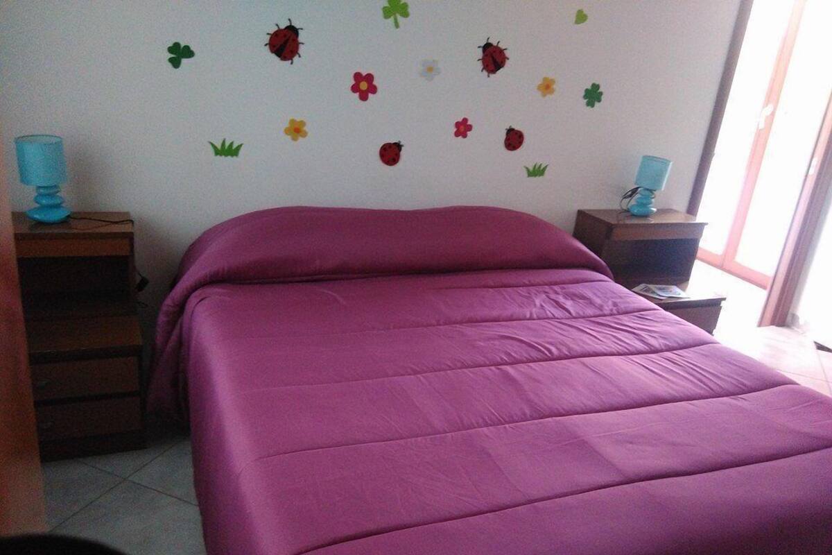 Une chambre à coucher avec un grand lit, une commode et une table de chevet. Les murs sont décorés de motifs floraux et de coccinelles.
