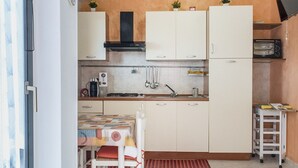 Et kompakt køkken med hvide skabe, en komfur og et lille spiseområde med et bord og stole.