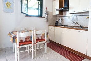 A kitchen with a stove, sink, and cabinets. There is a dining table with chairs and a window above it.