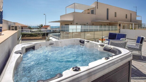 A hot tub with a glass enclosure, a seating area with chairs, and a building with a flat roof in the background. - Lovely apartment in Marina di Ragusa (Marina di Ragusa)
