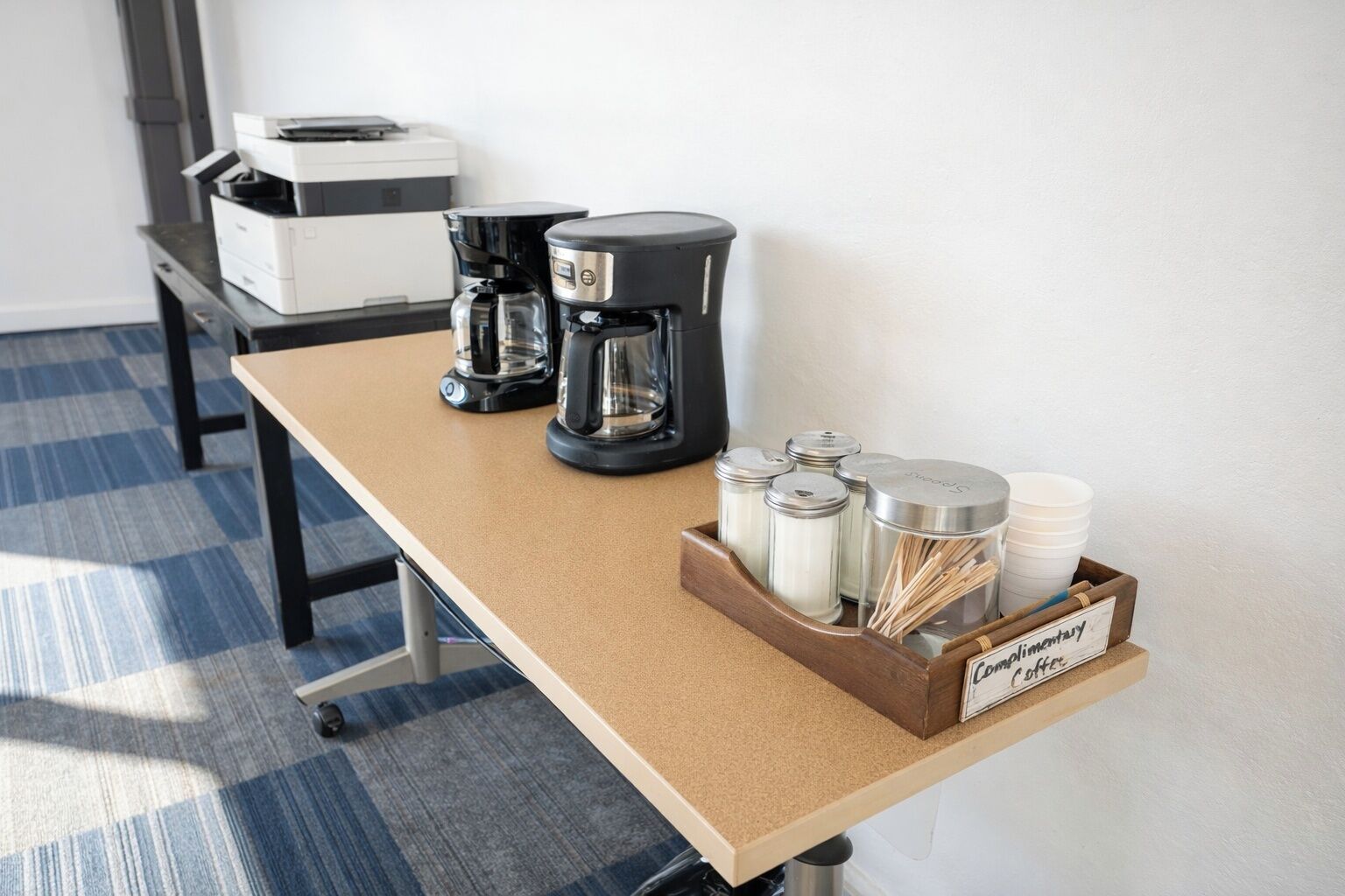 A coffee station with a coffee maker, a grinder, and a container labeled 'Complimentary Coffee.'