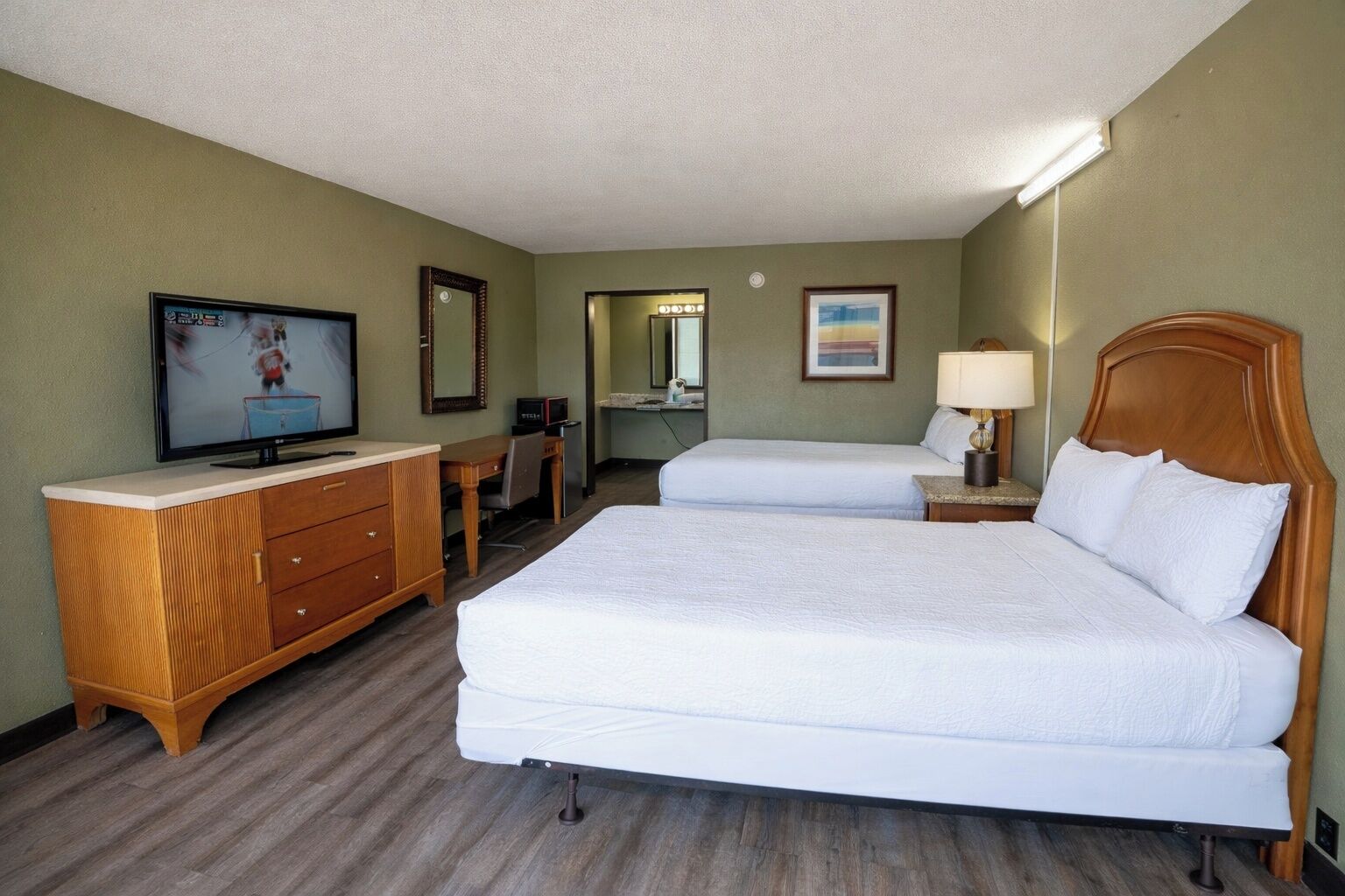 A hotel room with two beds, a television, a desk, and a mirror.