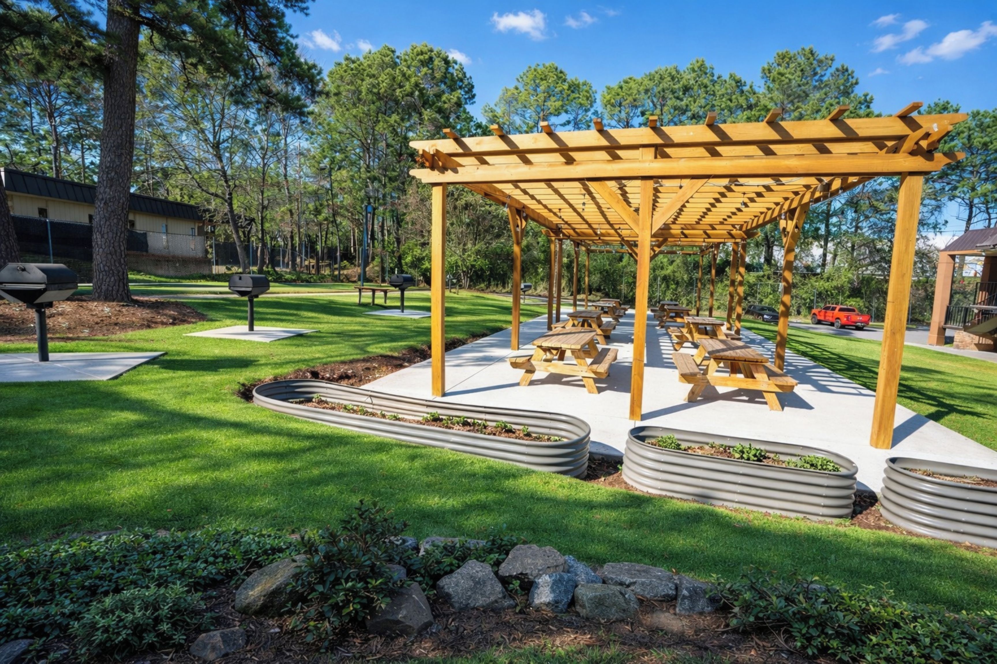 A covered outdoor seating area with picnic tables, surrounded by well-maintained grass and stone planters.