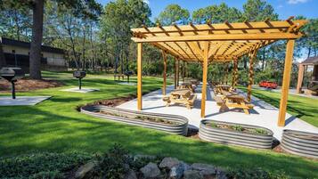 A covered outdoor seating area with picnic tables, surrounded by well-maintained grass and stone planters.