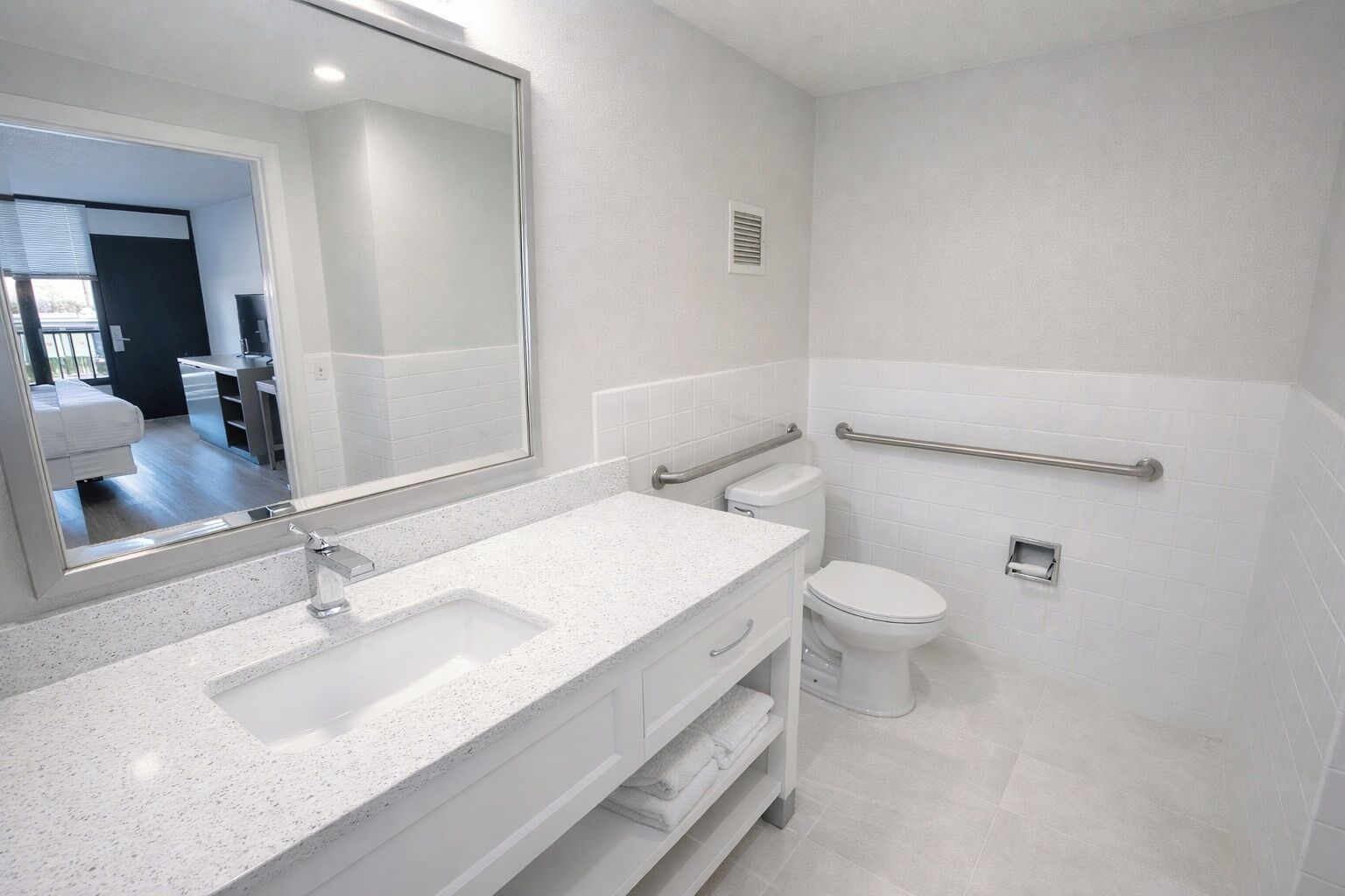 Uma casa de banho moderna com um lavatório branco, um espelho grande, uma sanita e um apoio de segurança.