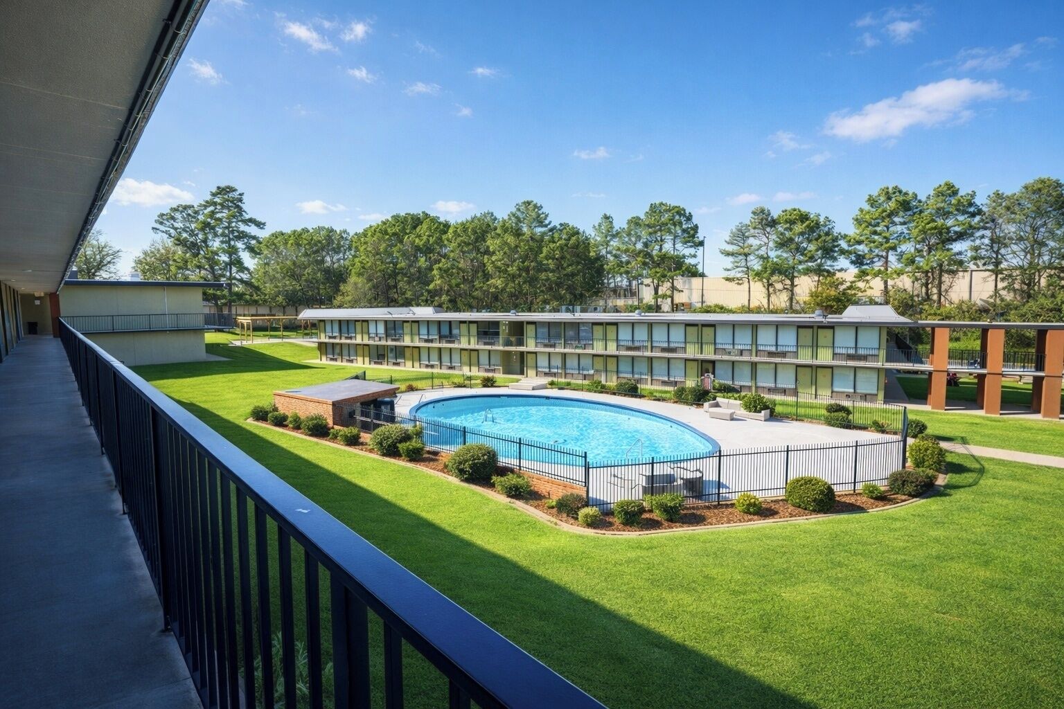 A hotel with a swimming pool, a covered walkway, and a view of the surrounding greenery.