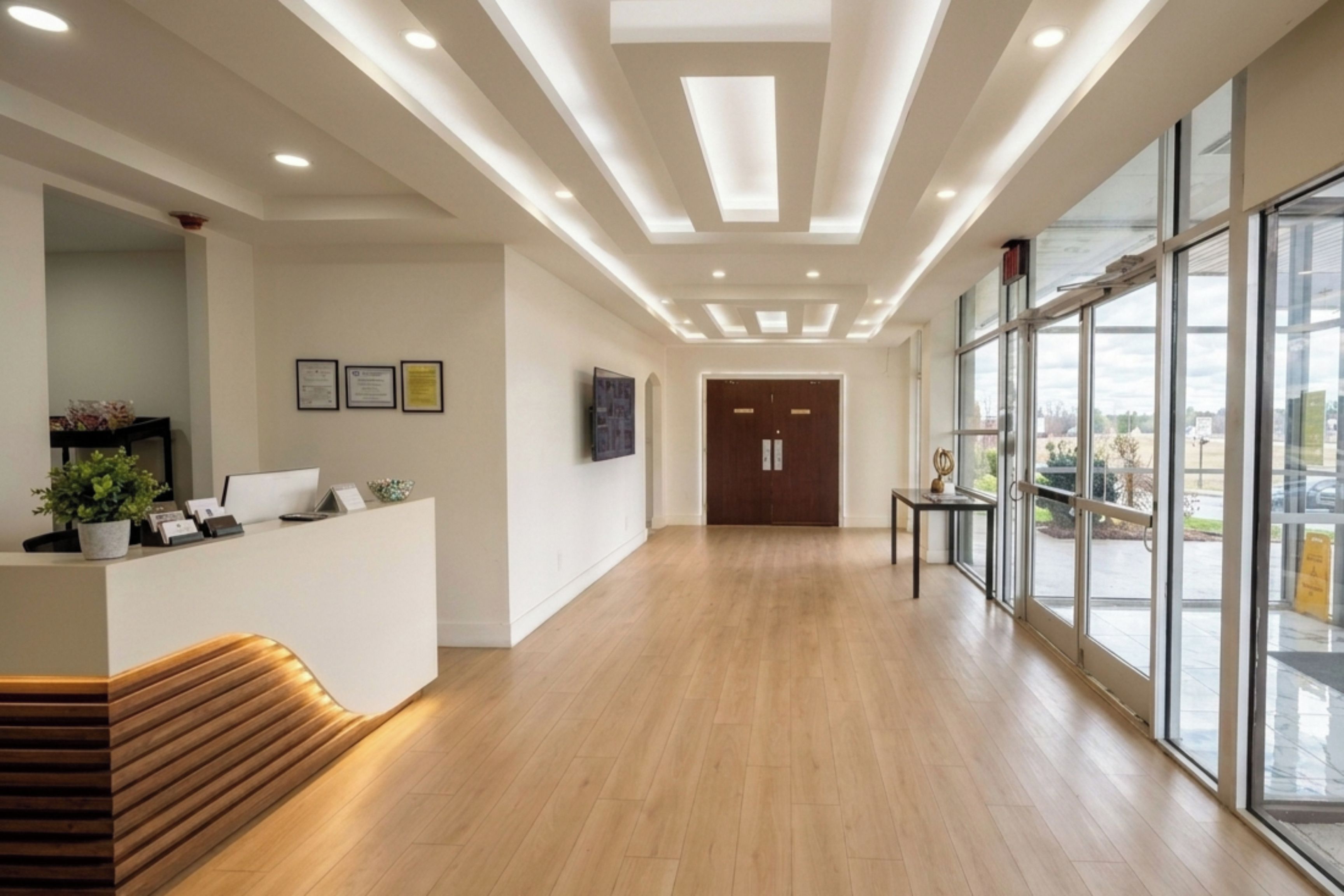 A reception area with a wooden bench, a reception desk, framed certificates on the wall, and a large window offering a view outside.
