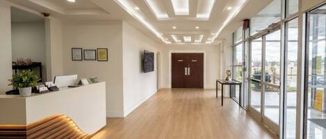 A reception area with a wooden bench, a reception desk, framed certificates on the wall, and a large window offering a view outside.