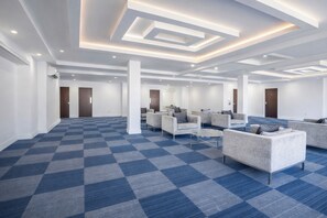 Um hall de hotel espaçoso com carpete quadriculado, área de estar com sofás e design de teto moderno.