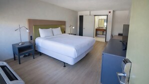 A hotel room with a bed, bedside tables, a desk, a mirror, and a bathroom door. - 1st Place Hotel Decatur I-20 East Atlanta (Decatur)