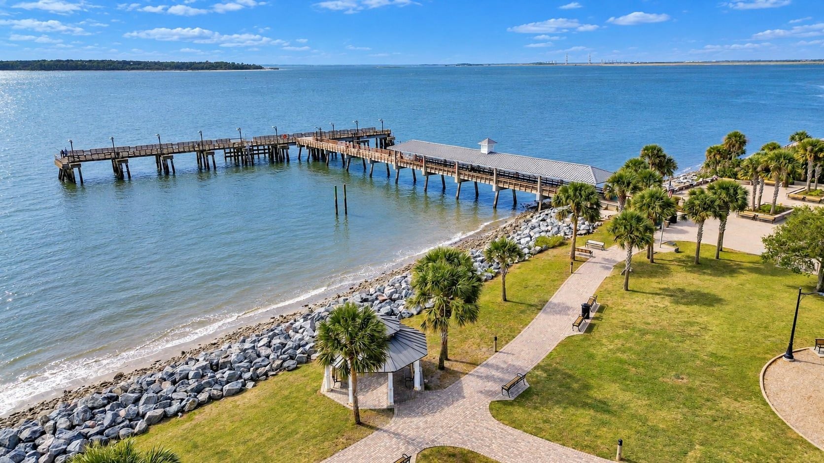 A pier extending into calm waters, a grassy area with benches, and a gazebo.