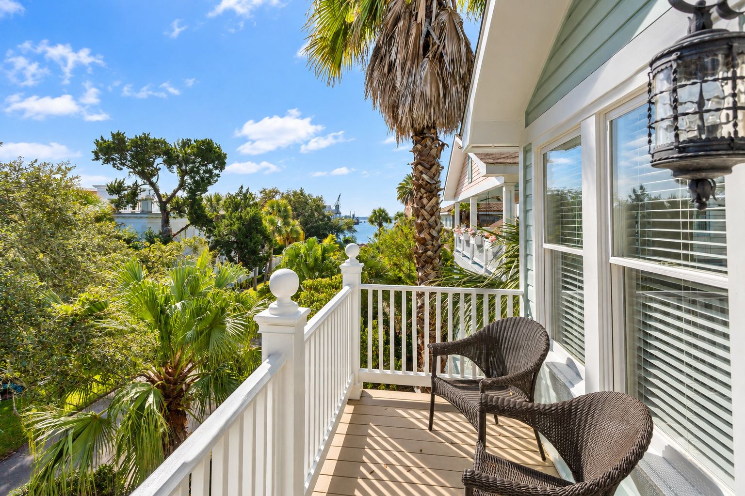 A balcony with wicker chairs, a white railing, and a view of the ocean and greenery.