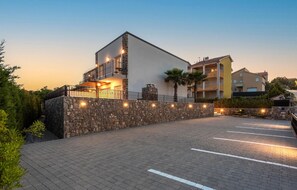 Un edificio moderno con fachada de piedra, un balcón y un estacionamiento.