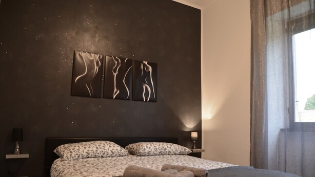 A modern bedroom with a large bed, patterned pillows, and a wall-mounted abstract art piece. - A Gray & Sexy Apartment in Rome (Roma)