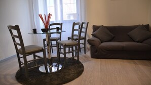 A living room with a brown sofa, two wooden chairs, a glass table with a black coaster, and a decorative vase with red sticks. - A Gray & Sexy Apartment in Rome (Roma)