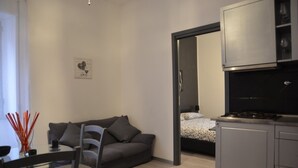 A compact living space with a kitchenette, a sofa, a dining table, and a bed with a patterned bedspread. - A Gray & Sexy Apartment in Rome (Roma)