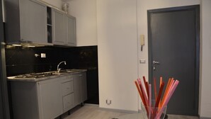 A modern kitchen with grey cabinets, a black backsplash, and a stainless steel stove. There is a glass vase with pencils on the floor. - A Gray & Sexy Apartment in Rome (Roma)