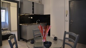 A modern kitchen with grey cabinets, a black countertop, and a dining area with a glass table and chairs. - A Gray & Sexy Apartment in Rome (Roma)