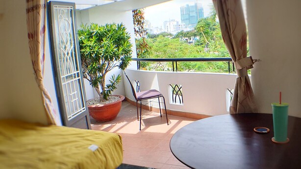 Een balkon met een bloempot, een stoel, een tafel en uitzicht op een stadsgezicht.