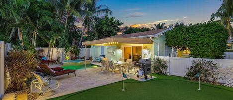 A backyard with a pool, patio furniture, and a barbecue area.