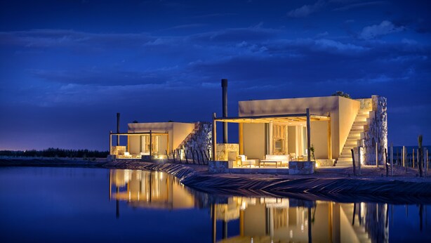 Una casa moderna con fachada de piedra, una escalera de madera y una piscina que refleja la edificación.