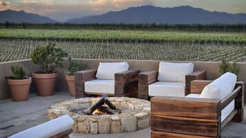 An outdoor seating area with a stone fire pit, wooden furniture, and potted plants.