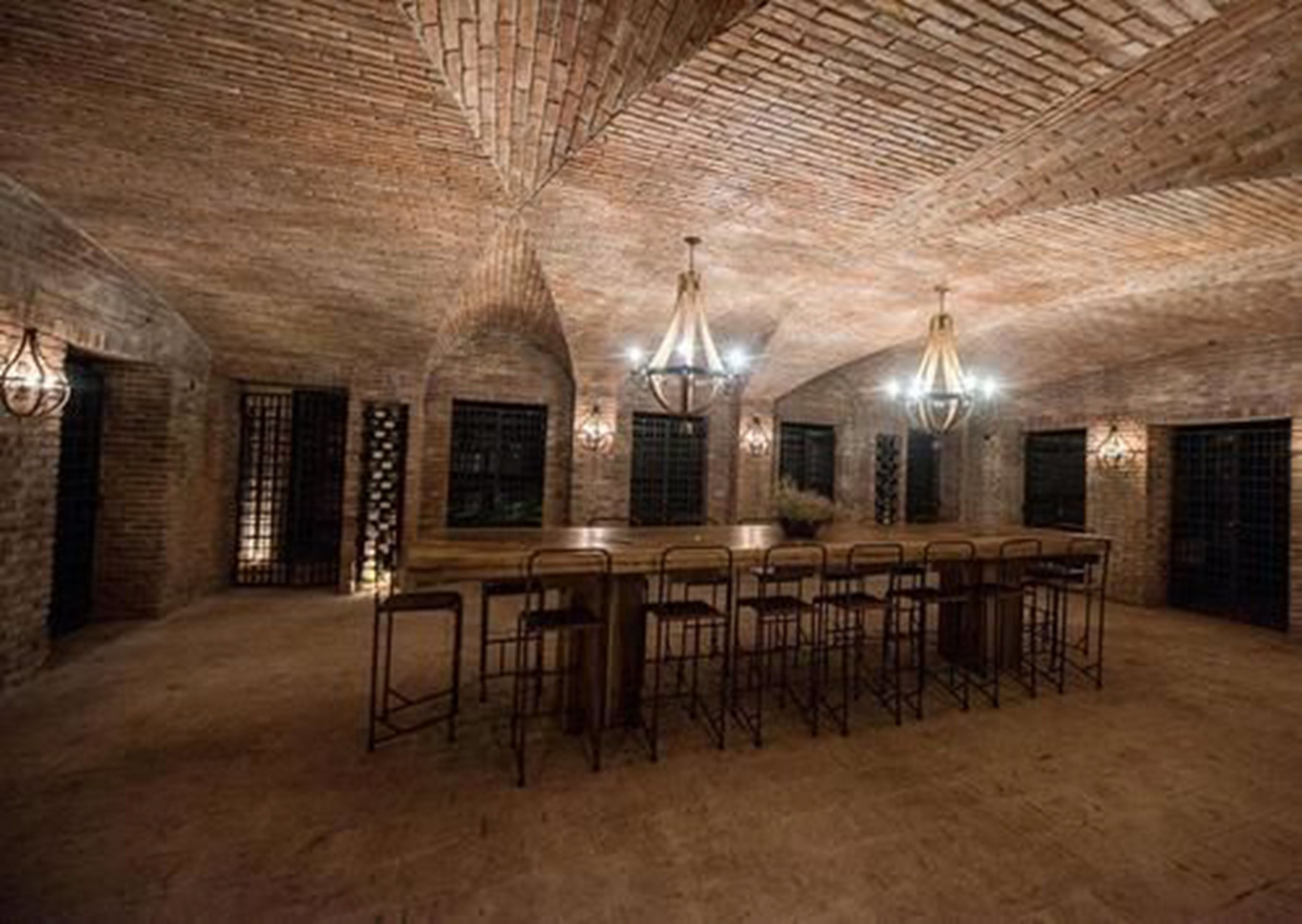 A spacious room with a long wooden table and multiple bar stools, featuring exposed brick walls and a vaulted ceiling.