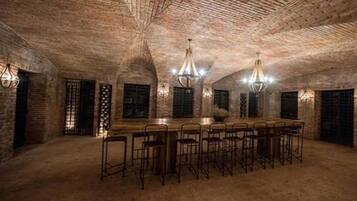 A spacious room with a long wooden table and multiple bar stools, featuring exposed brick walls and a vaulted ceiling.