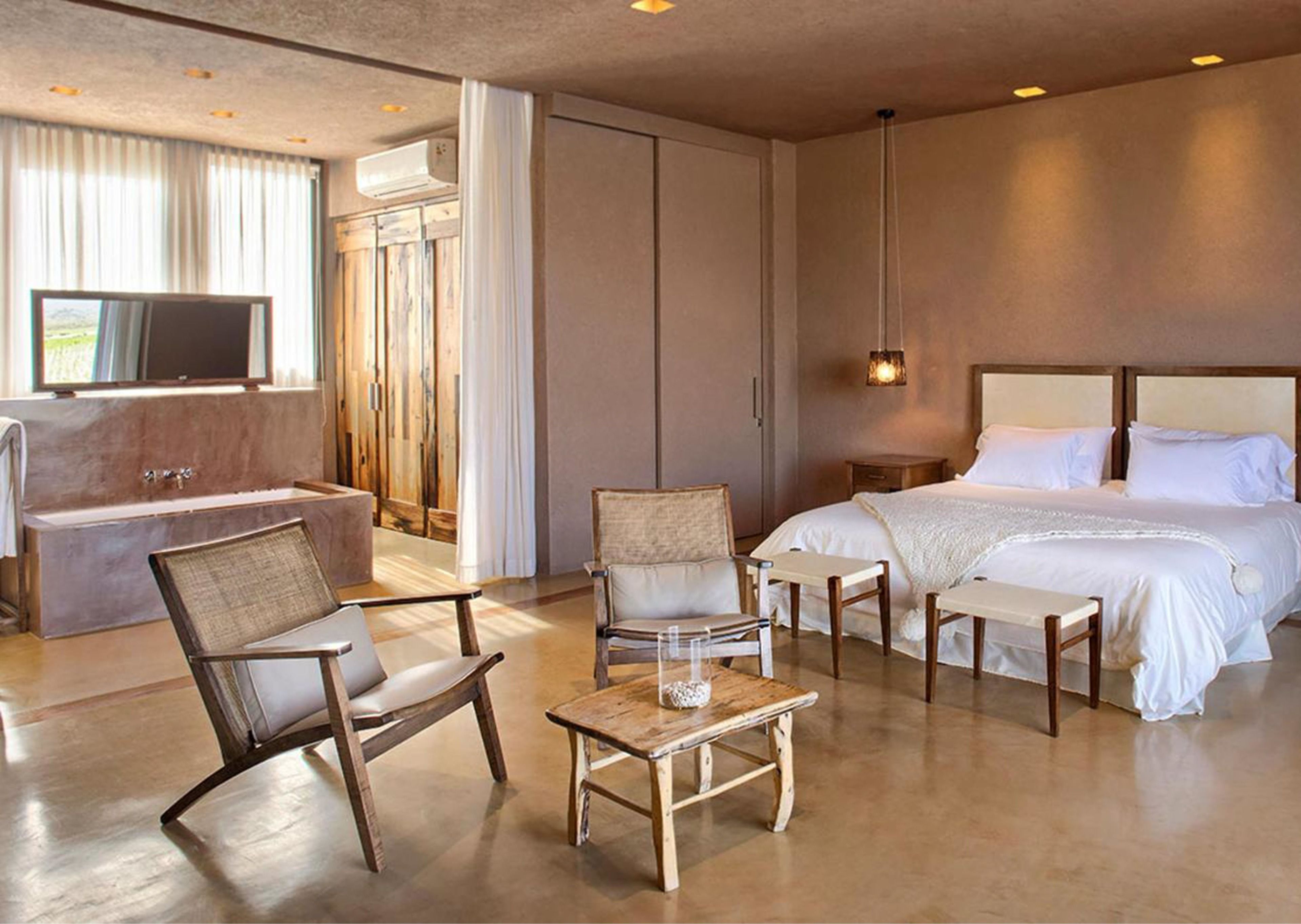 A modern hotel room with a large bed, a sitting area with a table and chairs, a bathtub, and a television.