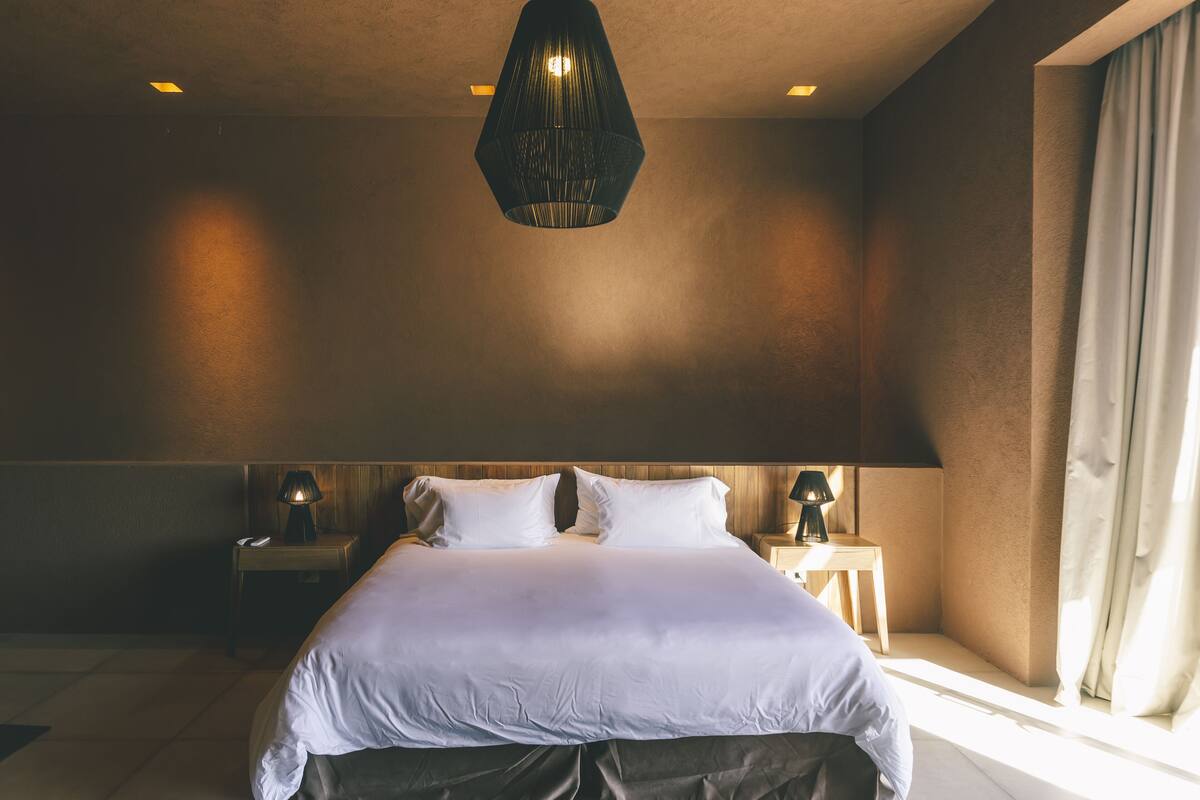 A large bed with white linens, two bedside tables with lamps, and a hanging light fixture.