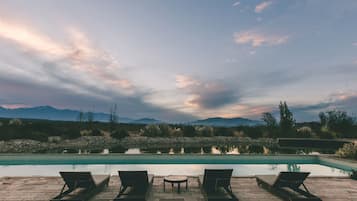 A poolside area with lounge chairs and a table, overlooking a calm pool and distant mountains.