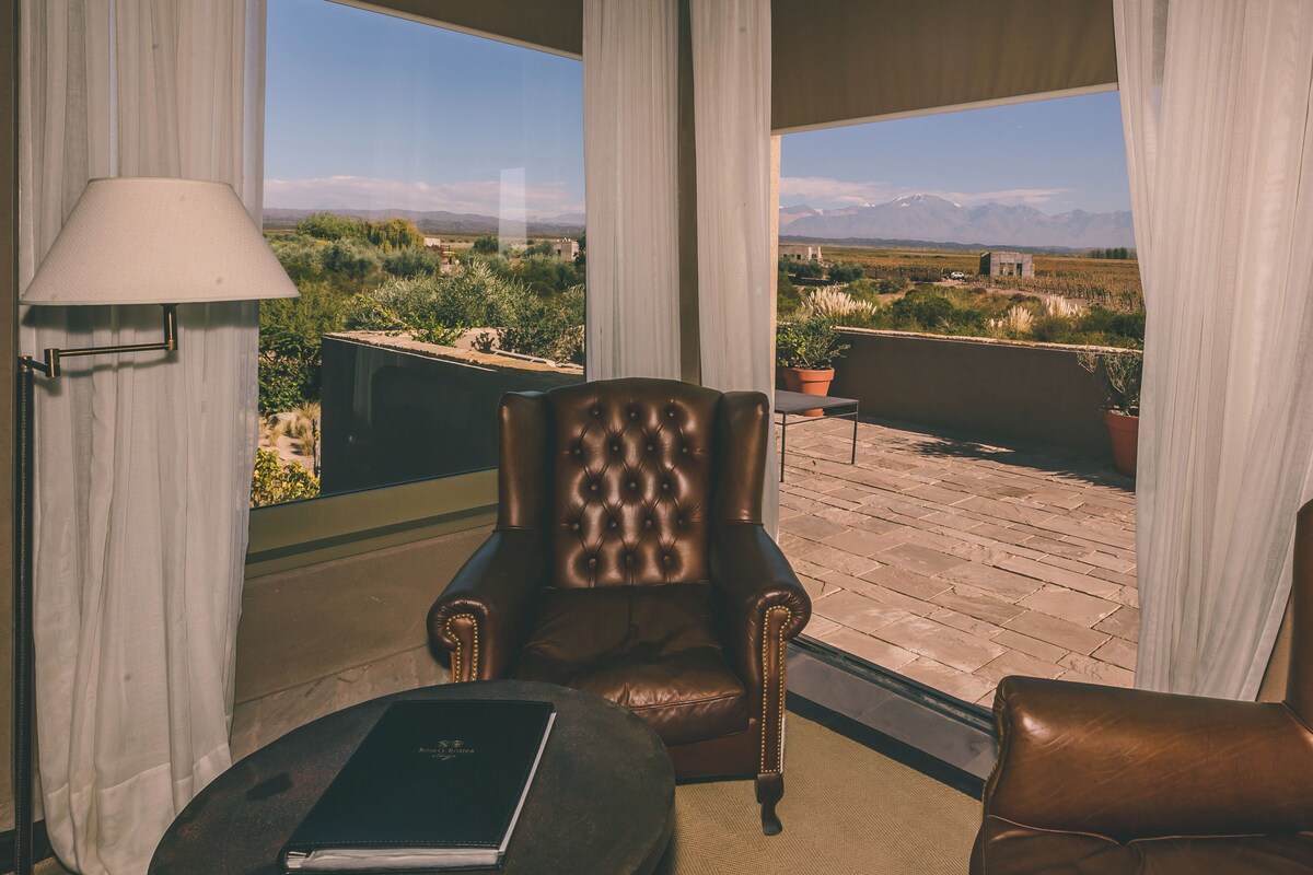Una habitación con un sillón de cuero, una pequeña mesa redonda con un libro y vistas a un paisaje montañoso a través de amplios ventanales.