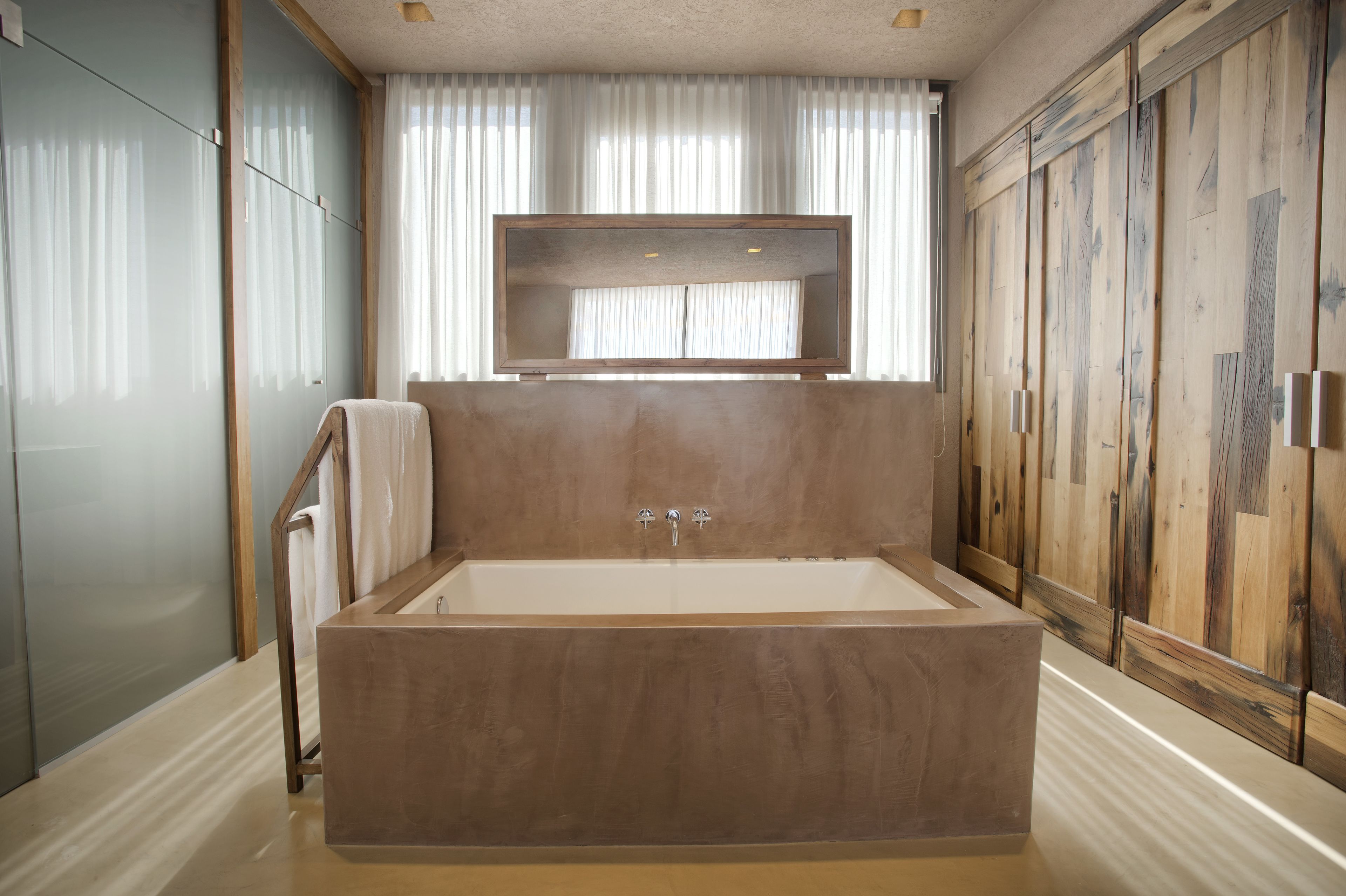 Un baño moderno con una bañera grande, paneles de madera y una ventana con cortinas translúcidas.