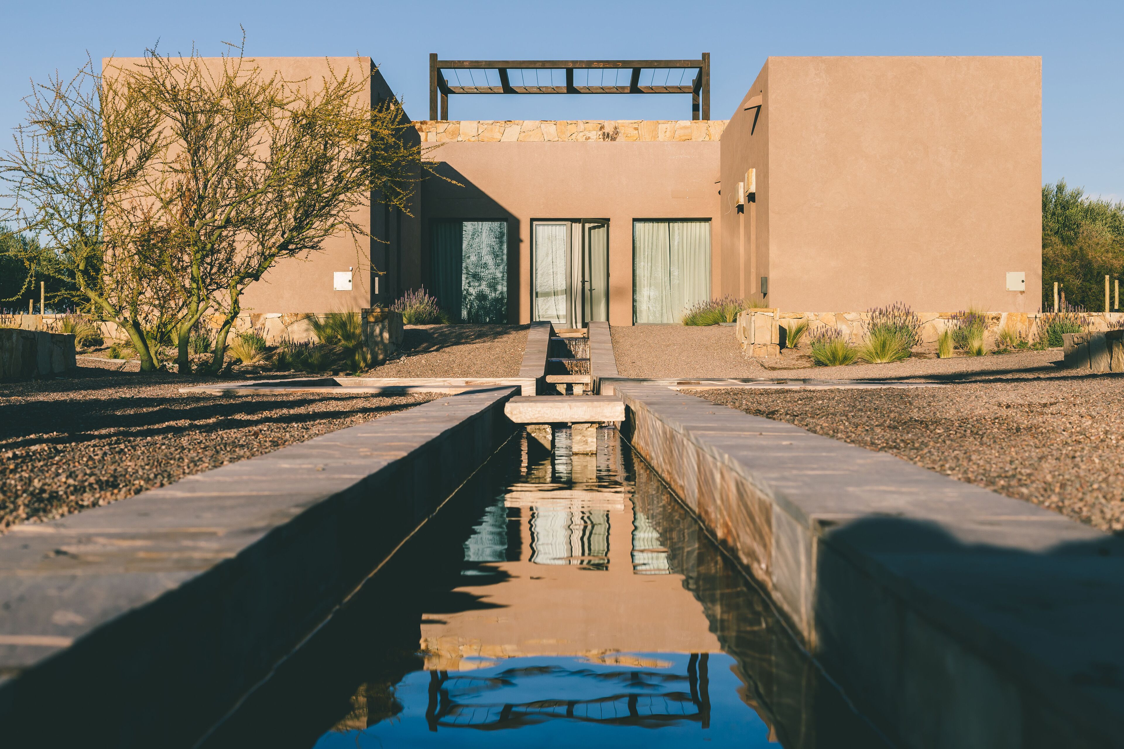 Un bâtiment moderne avec une piscine au premier plan, une pergola sur le toit et un ciel dégagé.