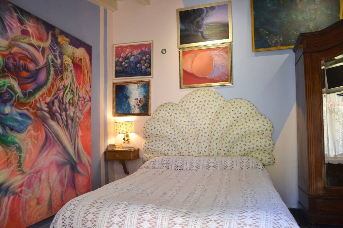Um quarto com cama, mesa de cabeceira, luminária e um quadro grande na parede.