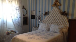 Un dormitorio con cama, mesita de noche, ventana con cortinas y pared con papel tapiz a rayas y adornos.