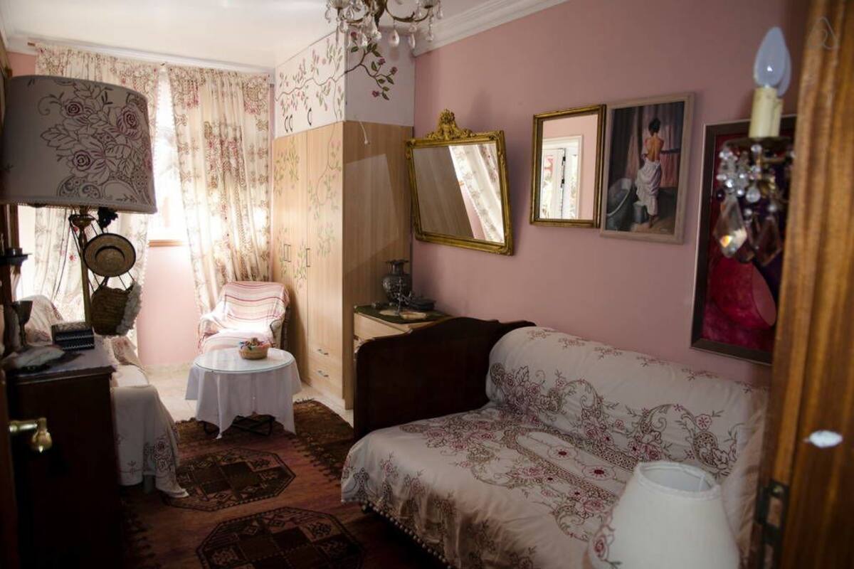 Um quarto aconchegante com sofá, mesa pequena, cadeira, abajur e espelho.