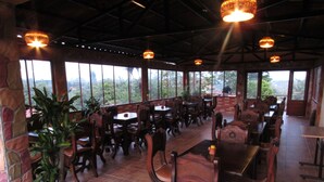 A restaurant with wooden tables and chairs, large windows, and hanging lights.