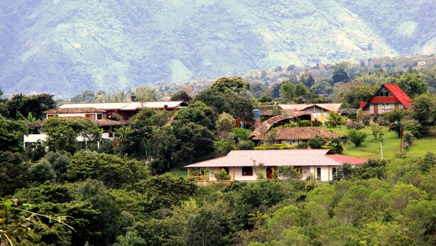 A rural village with traditional houses surrounded by lush greenery and hills in the background.