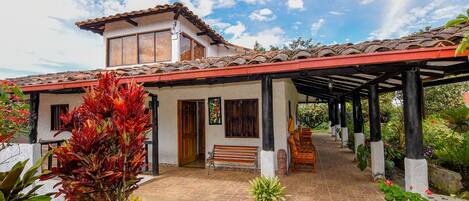 Una casa con techo de tejas, un porche cubierto y un jardín con plantas en macetas.