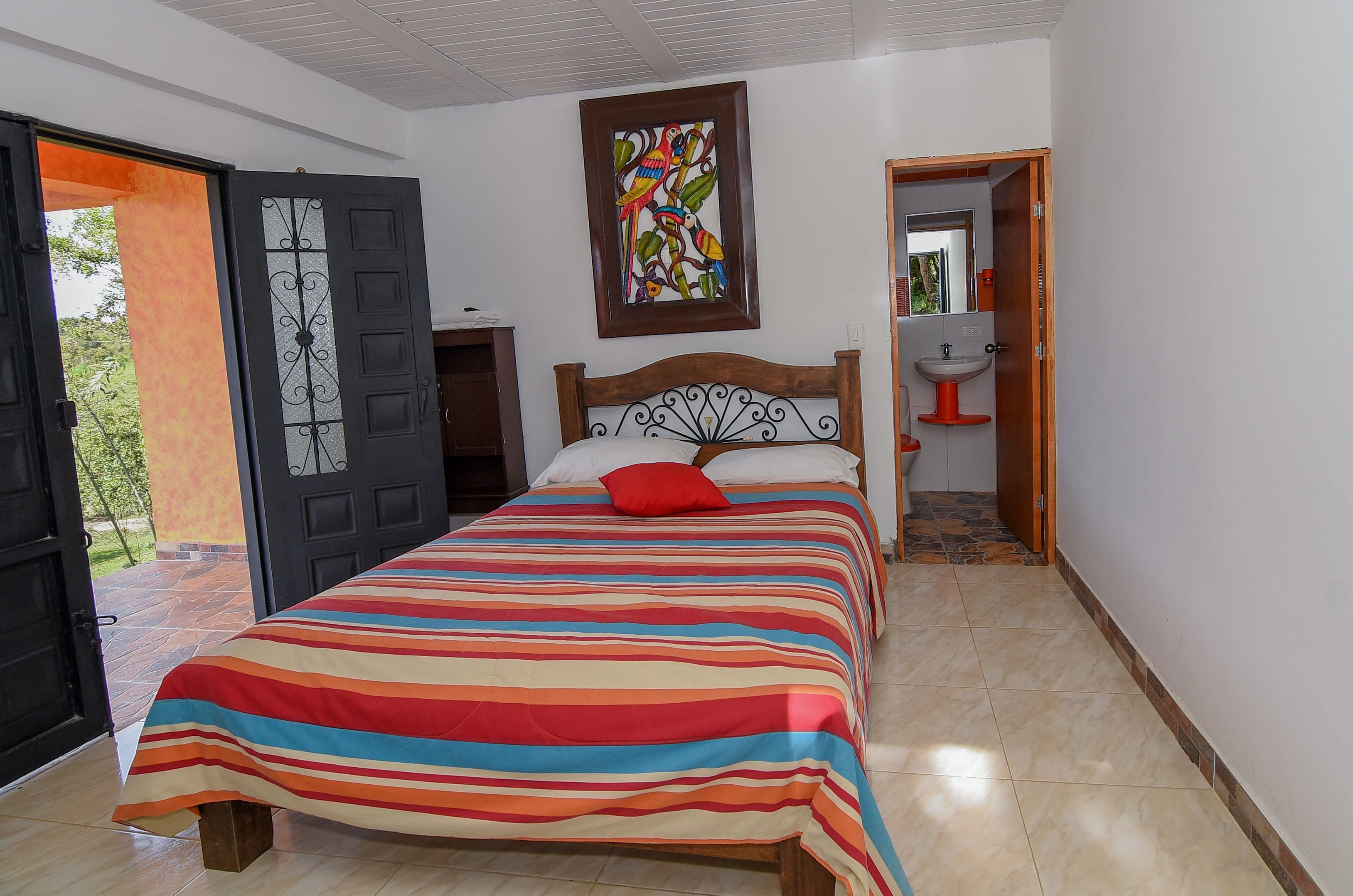 A bedroom with a bed, a door, a bathroom, and a view of the outdoors.