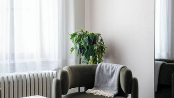 A modern living room with a green armchair, a small side table, a potted plant, and a large mirror on the wall.