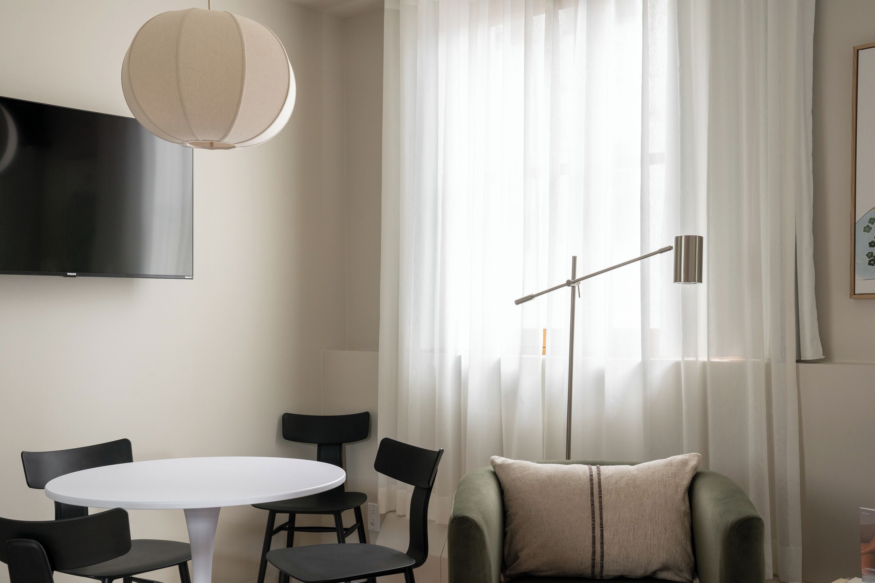 A modern living room with a round white table, black chairs, a green sofa, a flat-screen TV, and a pendant light.