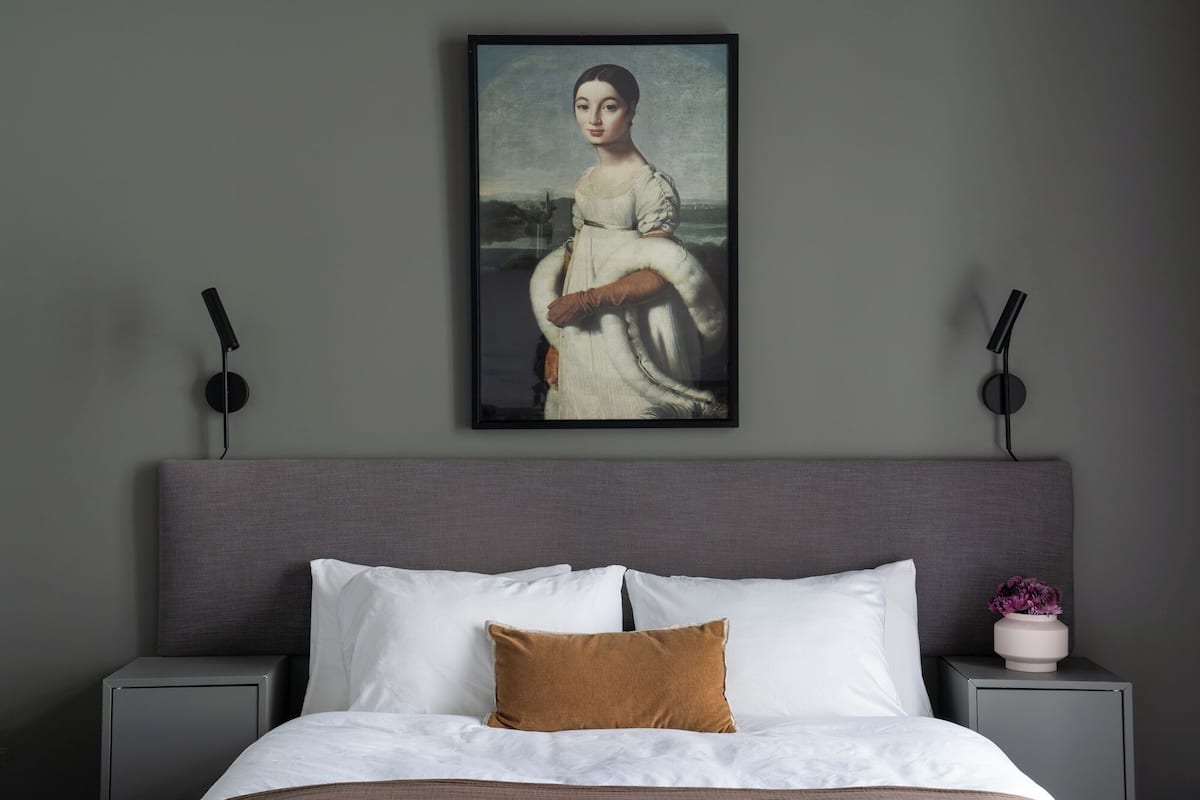A bedroom with a bed, a nightstand with a vase of flowers, and a painting on the wall.