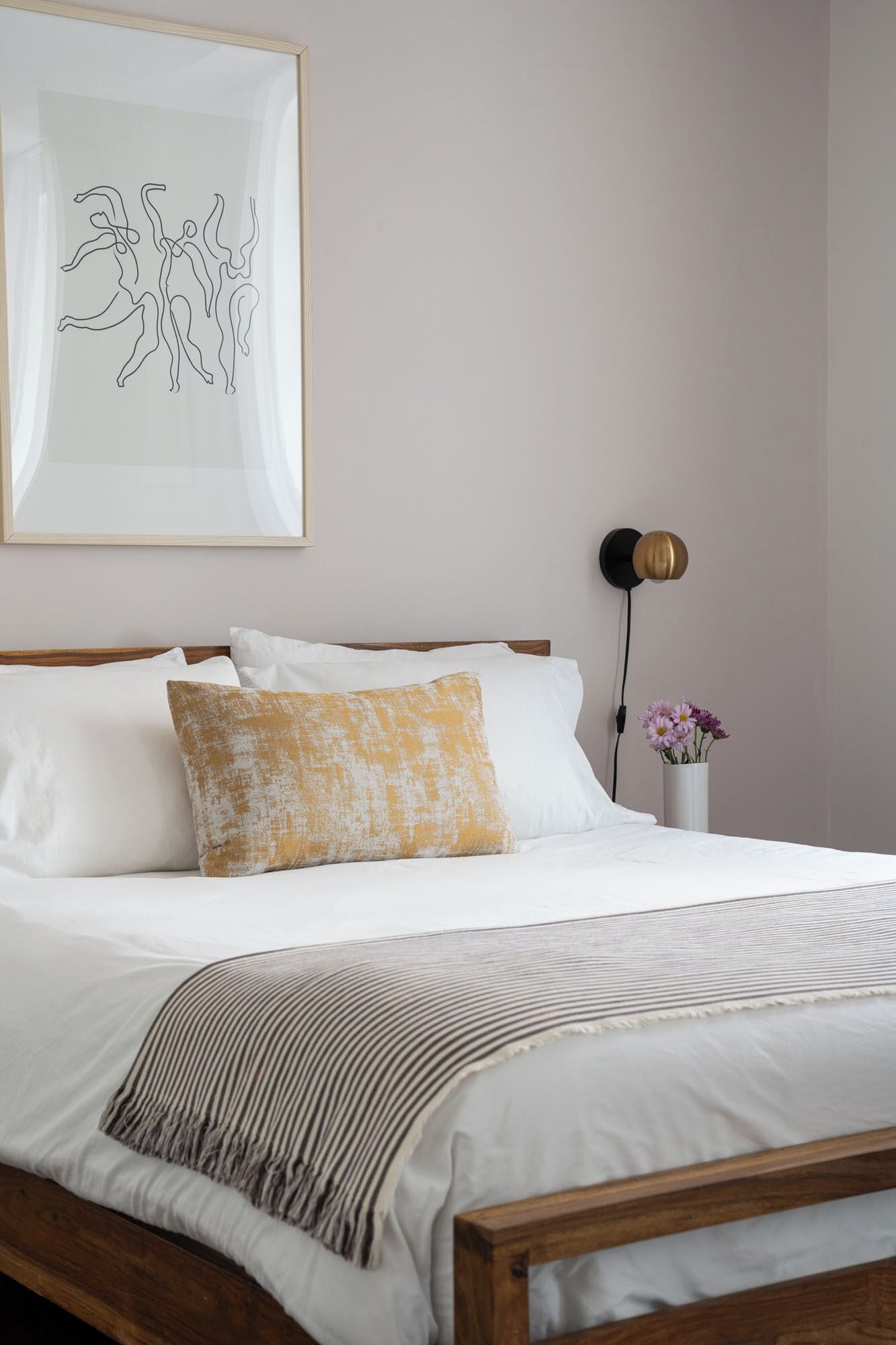A neatly made bed with white and yellow pillows, a striped throw blanket, and a framed abstract artwork above it.