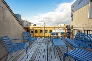 A rooftop deck with blue metal chairs and tables, a yellow building in the background, and a clear sky. - Maison Saint-Vincent (Montreal)