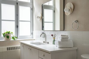 A bathroom with a white sink, a mirror, a towel rack, and a potted plant. - Maison Saint-Vincent (Montreal)