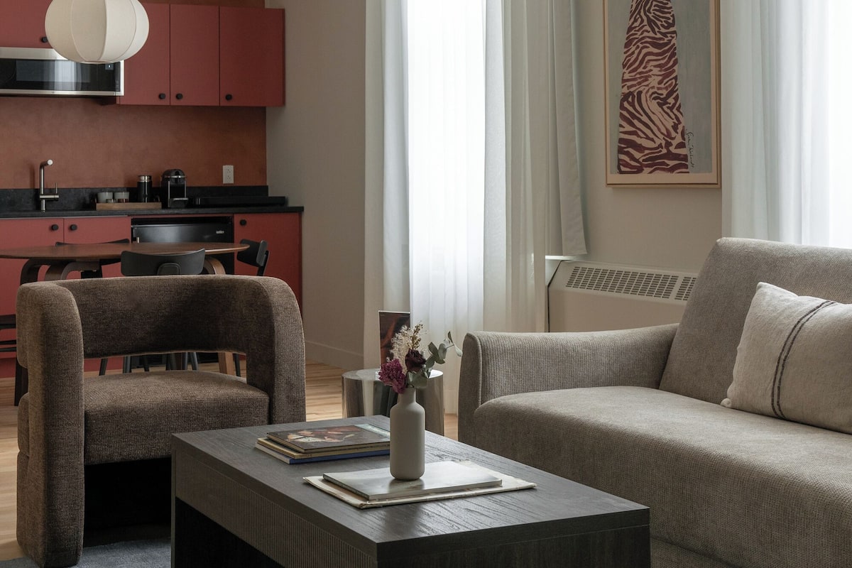 A modern living room with a sofa, a coffee table, and a dining area with chairs and a kitchen in the background.