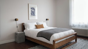 A bedroom with a wooden bed, white bedding, a gray throw blanket, and a framed artwork on the wall.