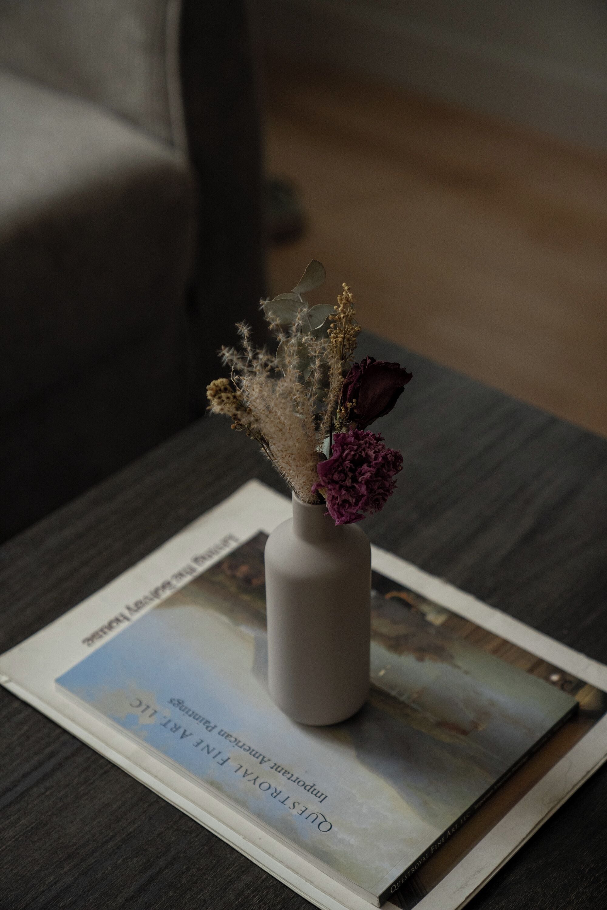 A vase with dried flowers on a table with a magazine.